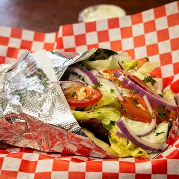 A gyro with lettuce, tomatoes, red onions, and sauce in a red and white checkered basket.