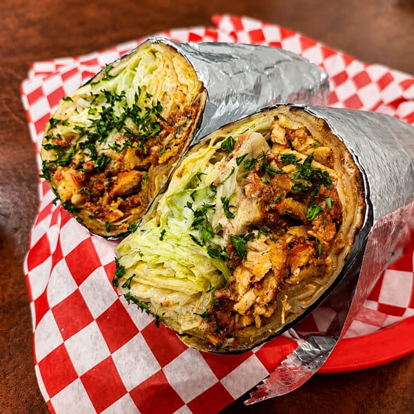 Two chicken shawarma wraps, cut in half, with lettuce and parsley, on red and white checkered paper.