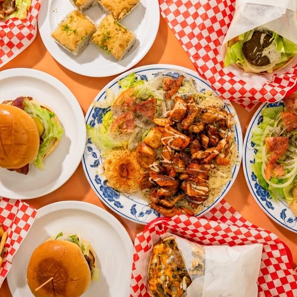 Overhead view of a feast of Middle Eastern dishes, including platters, wraps, burgers, and desserts.