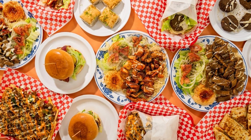 Overhead view of a feast of Middle Eastern dishes, including platters, wraps, burgers, and desserts.